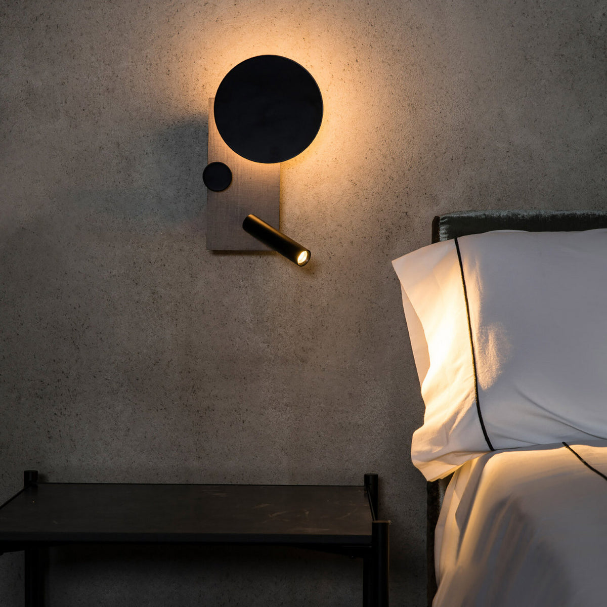 Applique murale noire et grise installée près d'un lit et d'une table de chevet