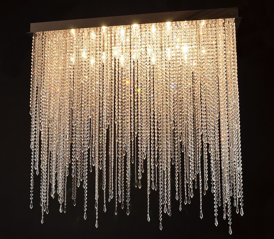 Lustre allumé, cascade de cristaux dorés suspendue à une plaque rectangulaire fixée au plafond.
