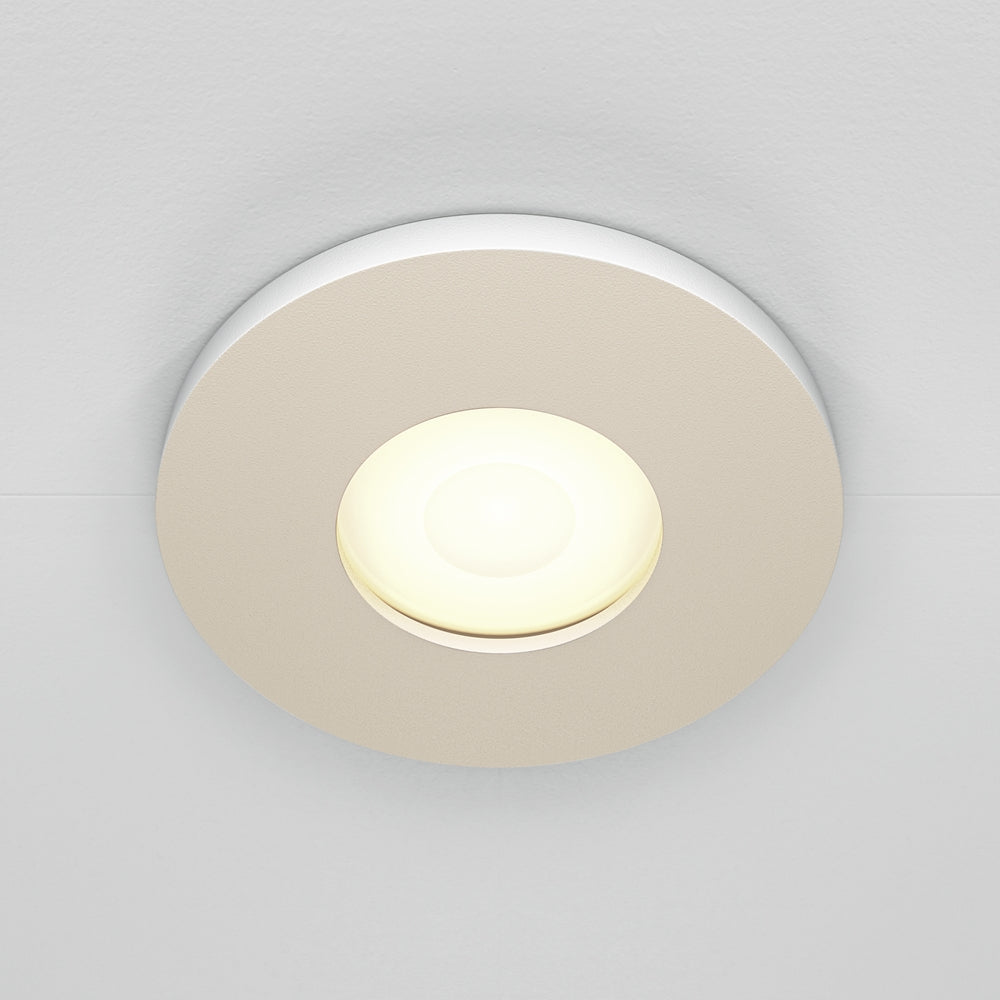 Spot encastré rond beige allumé, vue de face sur plafond blanc