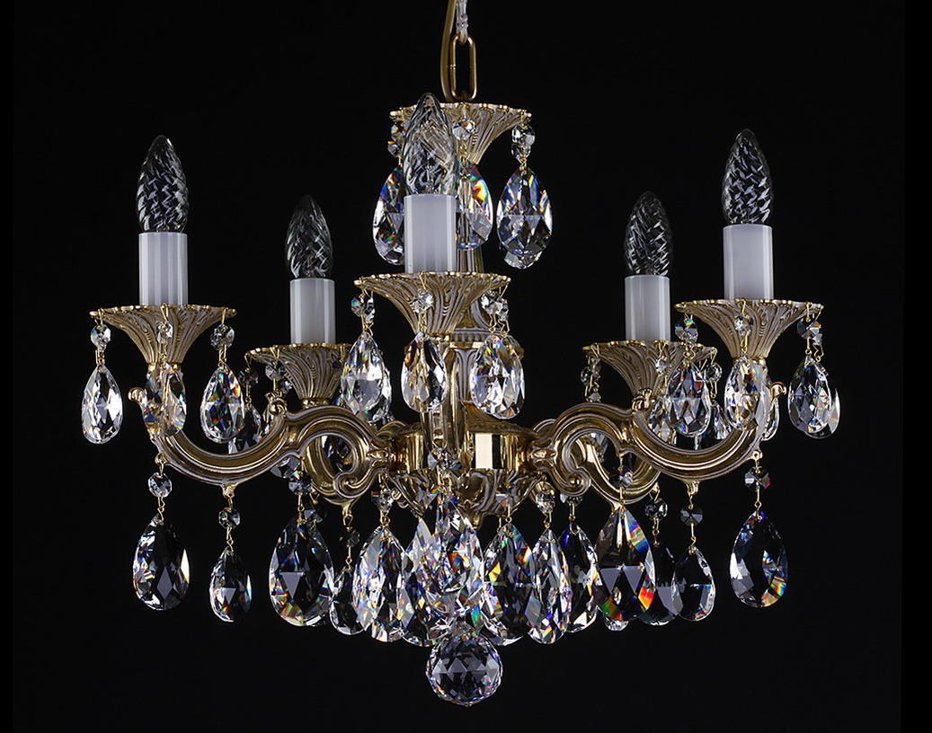 Lustre doré à six bras garni de cristaux taillés, photographié de face sur fond noir