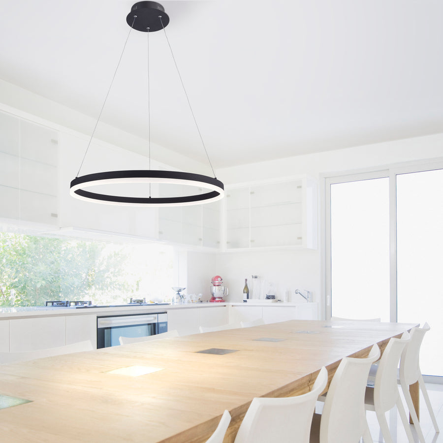 Suspension circulaire noire éclairant une table de cuisine en bois clair.