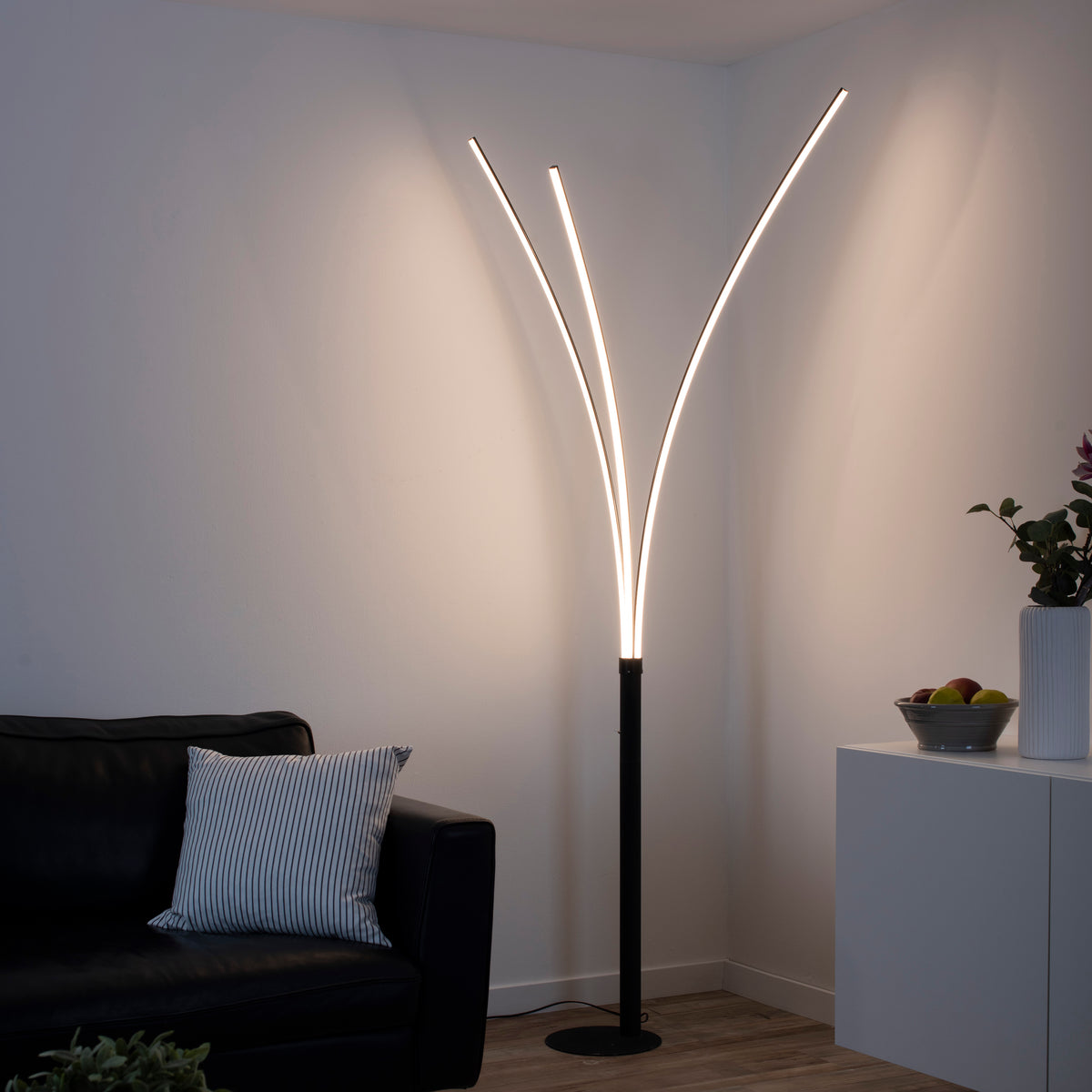Mise en ambiance dans un salon, lampadaire allumé près d'un canapé noir