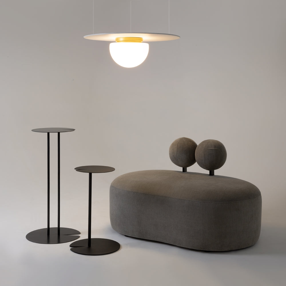 Mise en ambiance avec guéridons noirs et pouf gris, suspension allumée au-dessus.