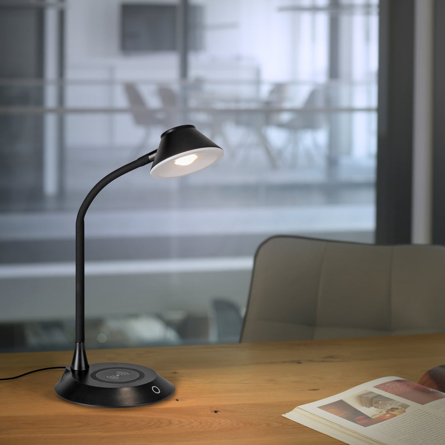 Lampe à poser noire allumée sur un bureau en bois dans un espace de travail