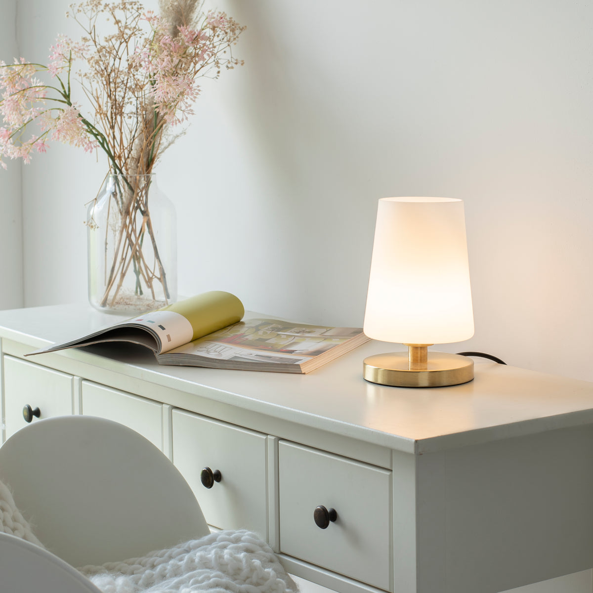 Mise en ambiance sur une commode blanche, près d'un vase de fleurs séchées et d'un magazine