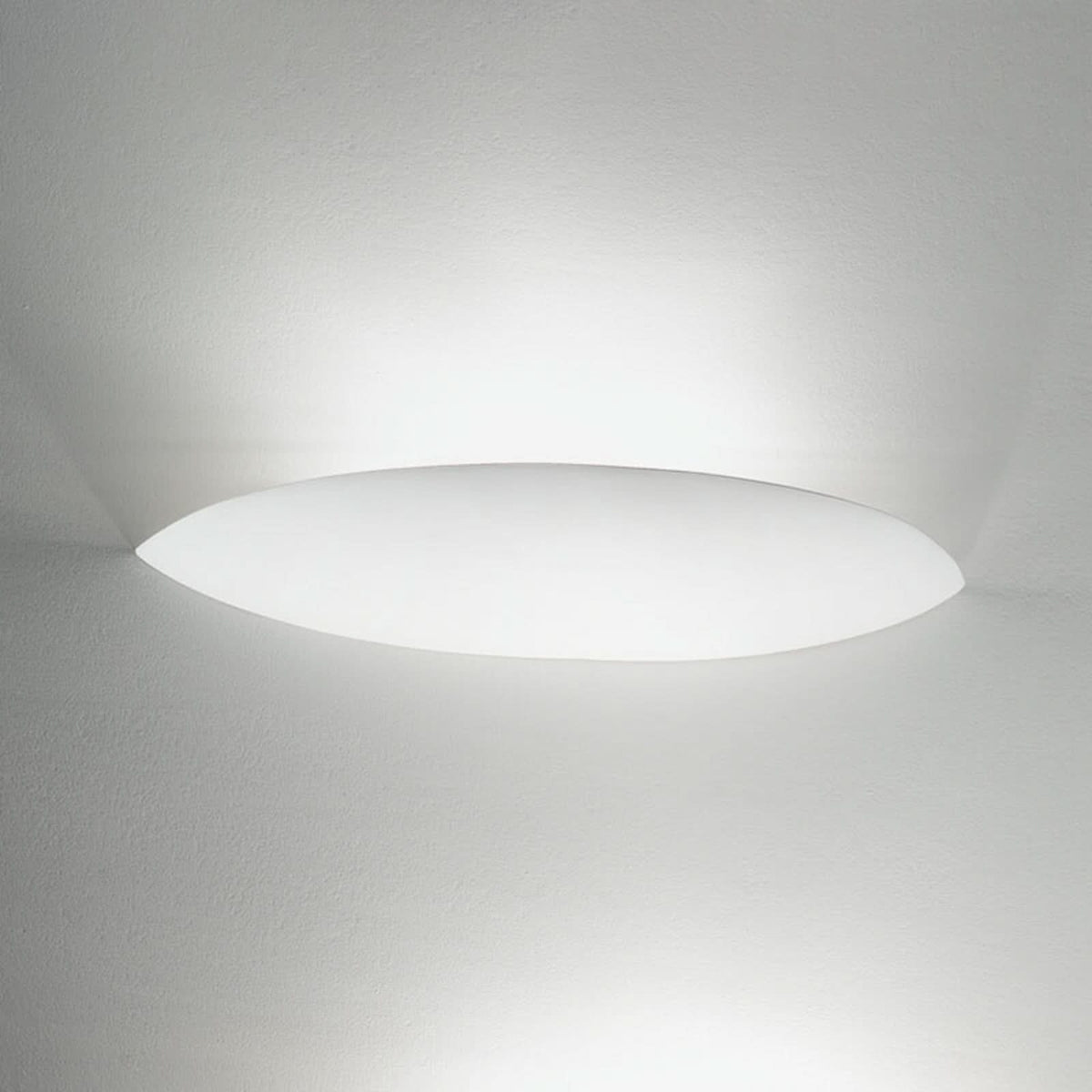 Applique murale ovale blanche allumée sur un mur blanc, lumière diffuse projetée autour