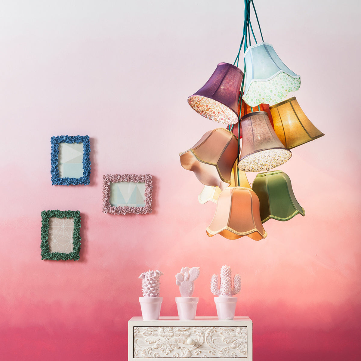 Mise en ambiance sur fond rose avec cadres et petites cactus sous la suspension.