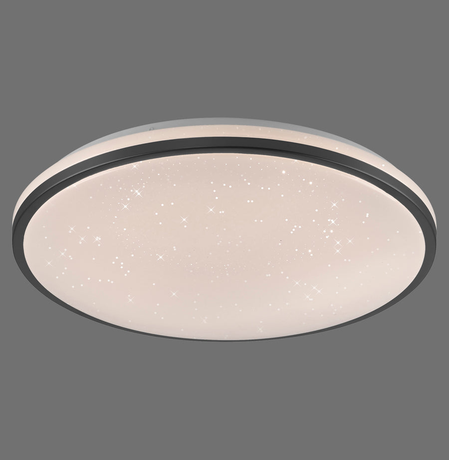 Luminaire rond de plafond allumé, bordure noire et diffuseur étoilé, sur fond gris.