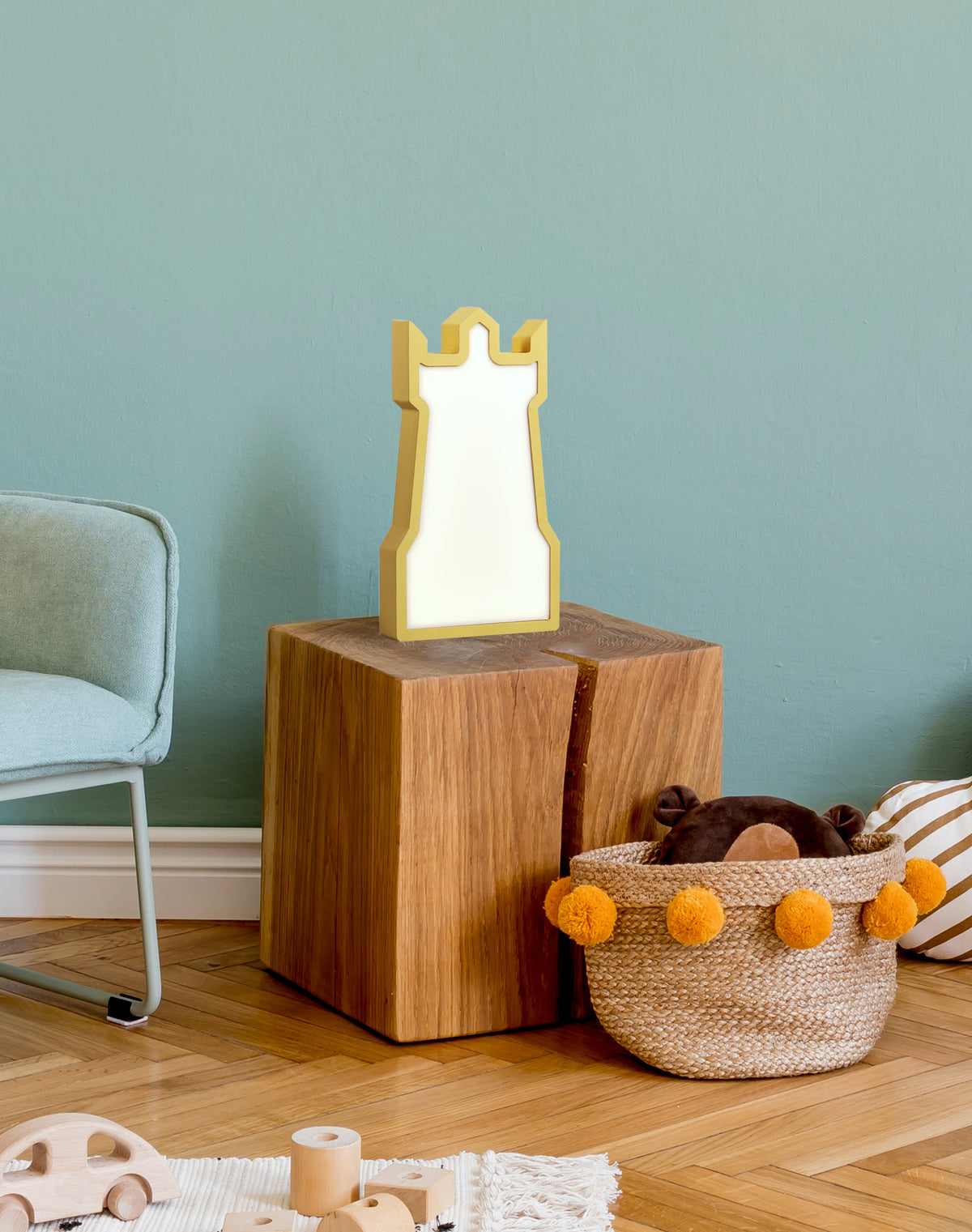 Lampe tour dorée posée sur un cube en bois dans une chambre d'enfant.