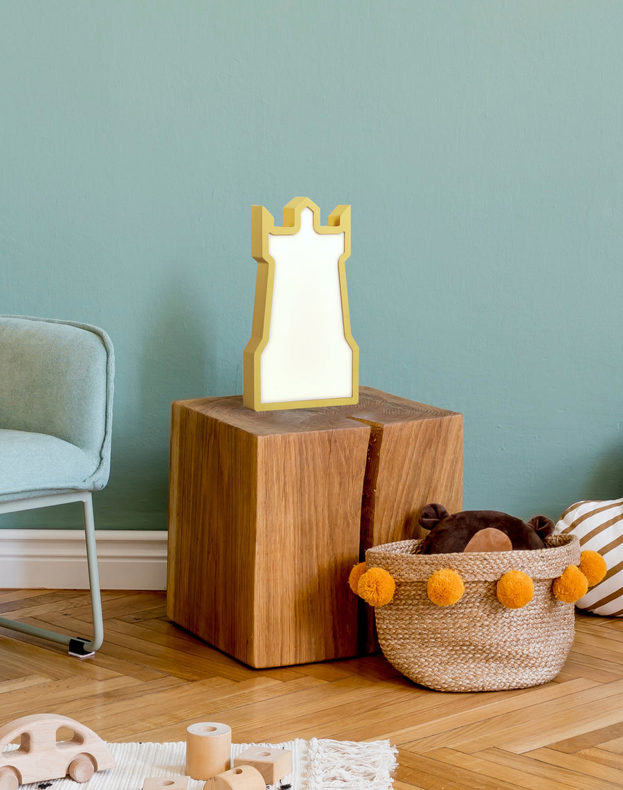Lampe tour dorée posée sur un cube en bois dans une chambre d'enfant.