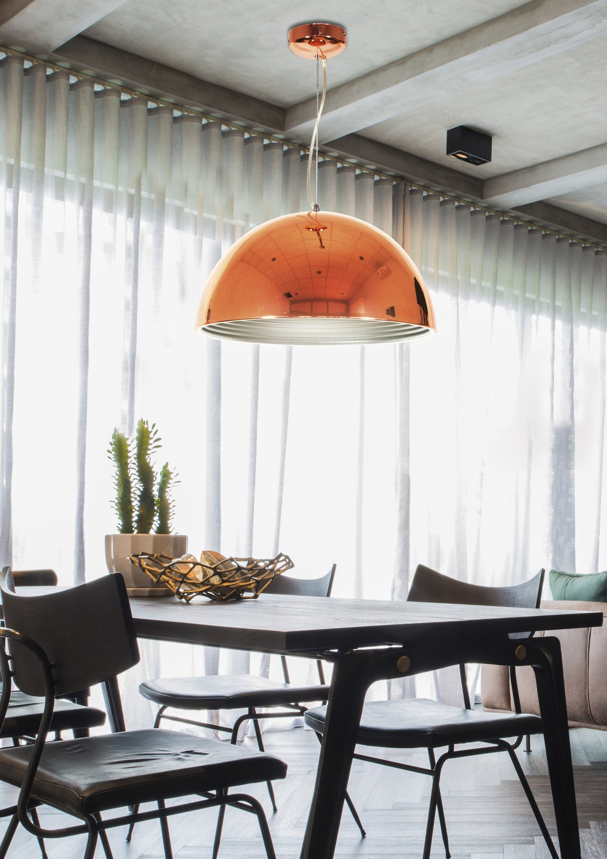 Luminaire cuivré suspendu au-dessus d'une table en bois, rideaux clairs
