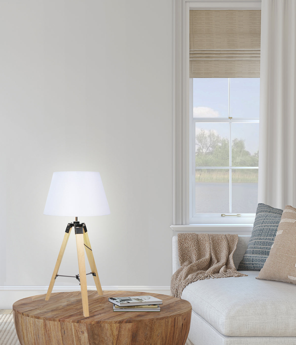 Lampe trépied allumée posée sur table basse en bois rond, près d'un canapé