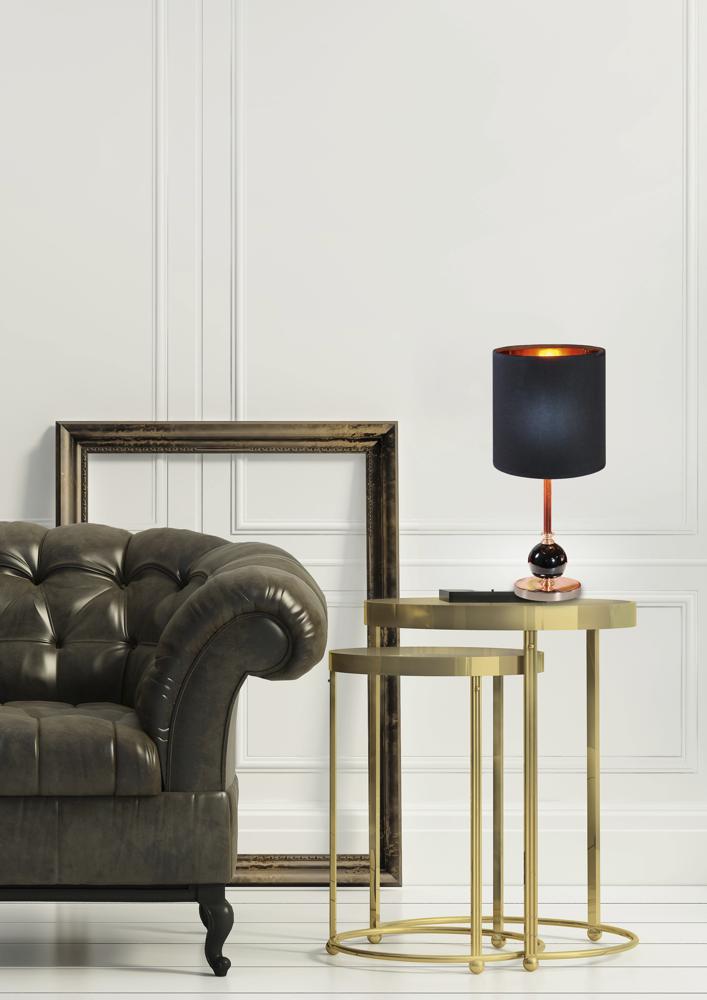 Mise en scène de la lampe noire sur table dorée, canapé capitonné et cadre.