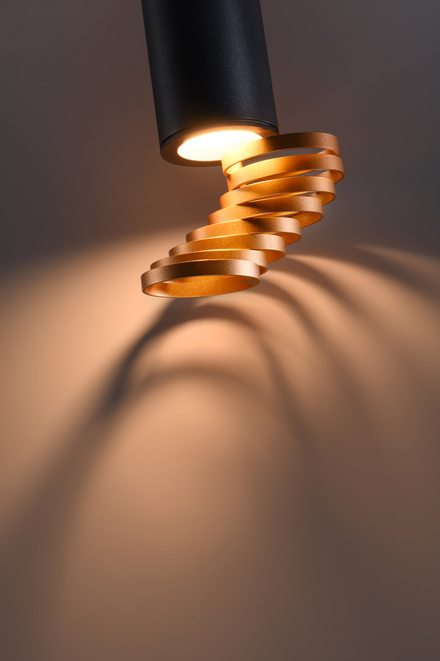 Gros plan du modèle noir éclairé, spirale dorée et ombres portées sur le mur