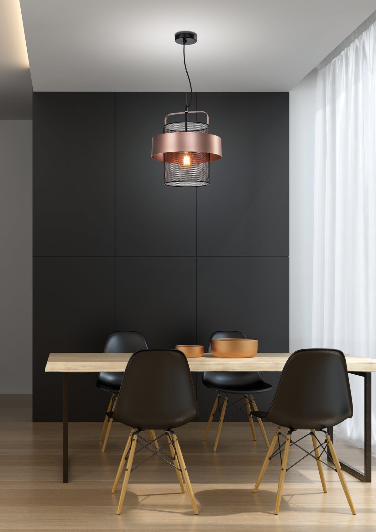 Suspension noire et cuivre installée au-dessus d'une table à manger en bois clair.