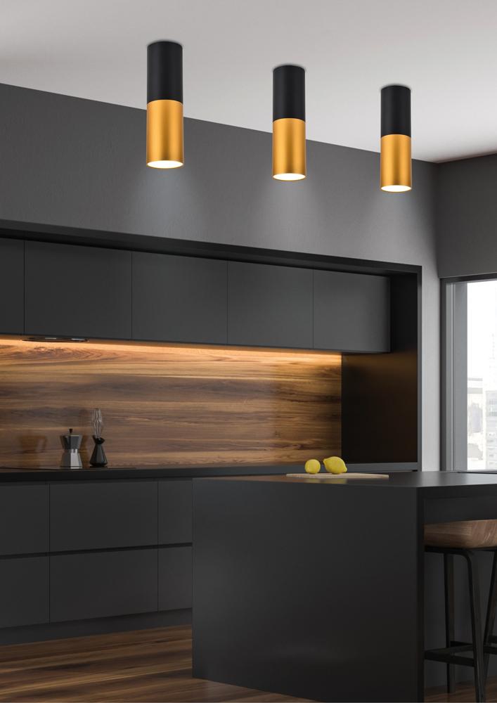 Vue rapprochée de trois spots plafond noir et or au-dessus d'un plan de travail sombre