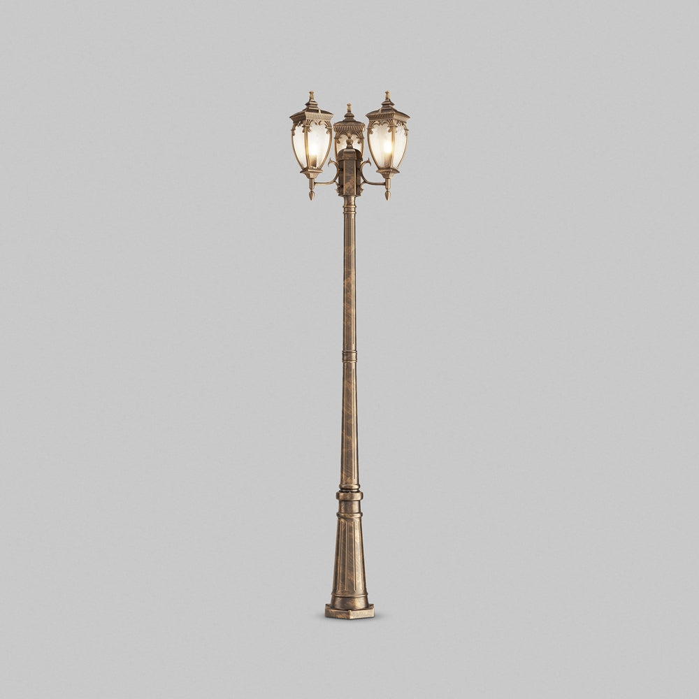 Lampadaire à trois lanternes classiques sur poteau festonné, vue de face sur fond gris.