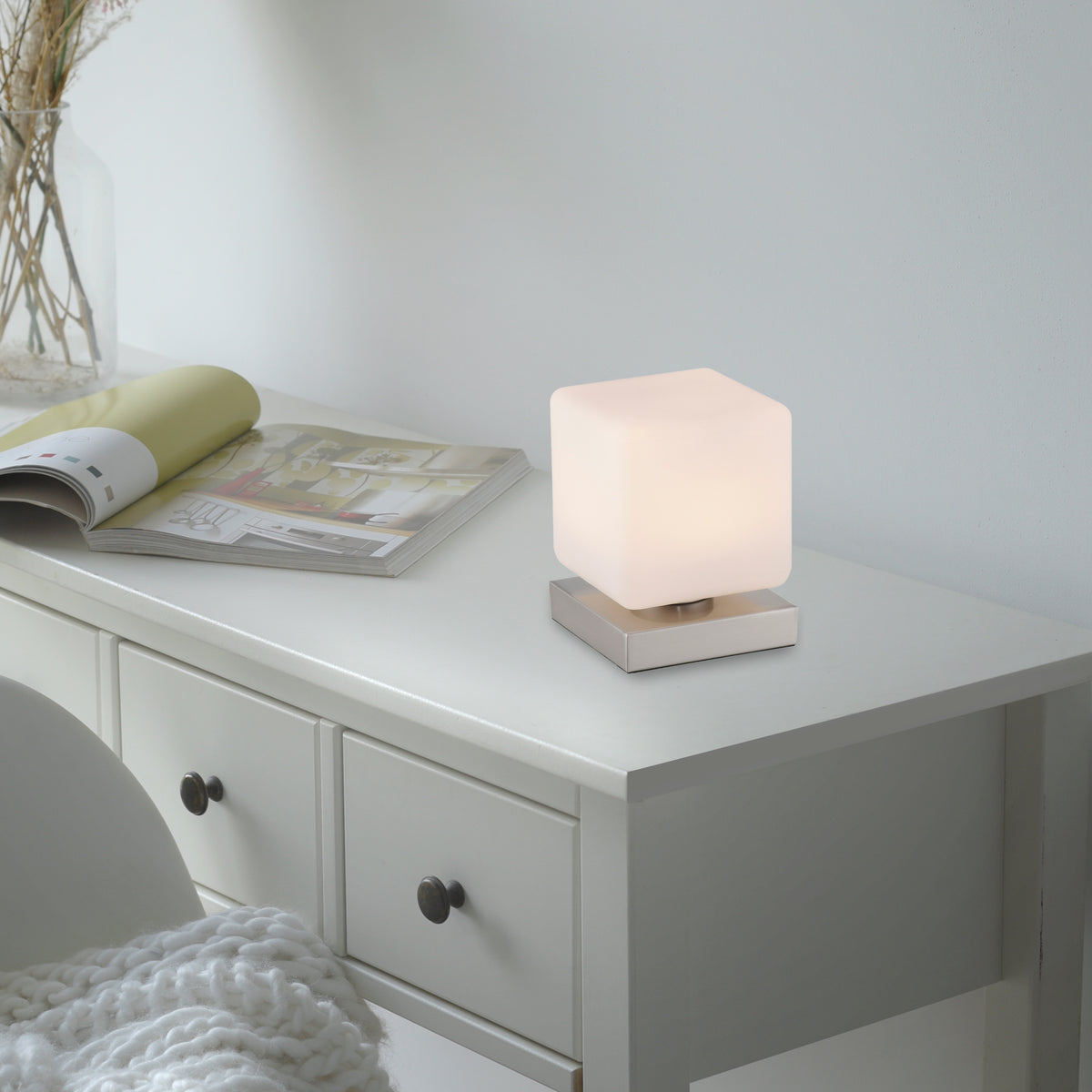 Mise en situation : lampe allumée posée sur une commode blanche près d'un magazine