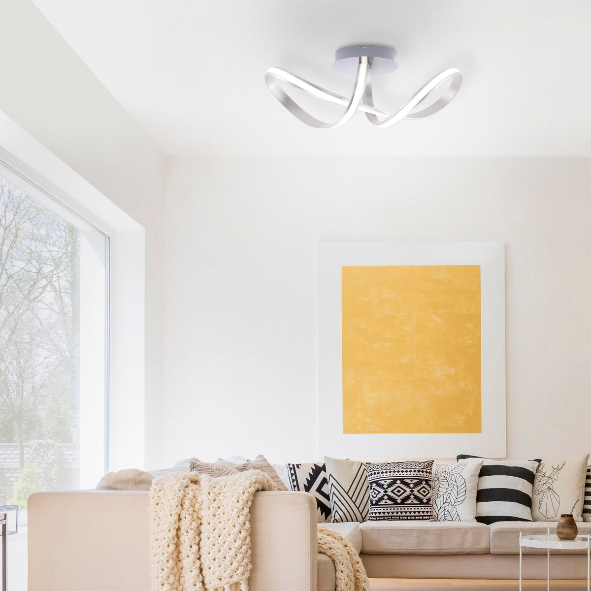 Mise en ambiance du plafonnier allumé dans un salon moderne, canapé beige et grand tableau jaune.