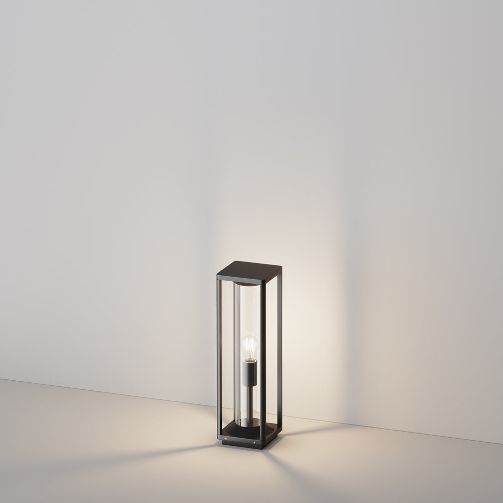 Lampadaire extérieur de face, cadre noir rectangulaire et cylindre de verre transparent.