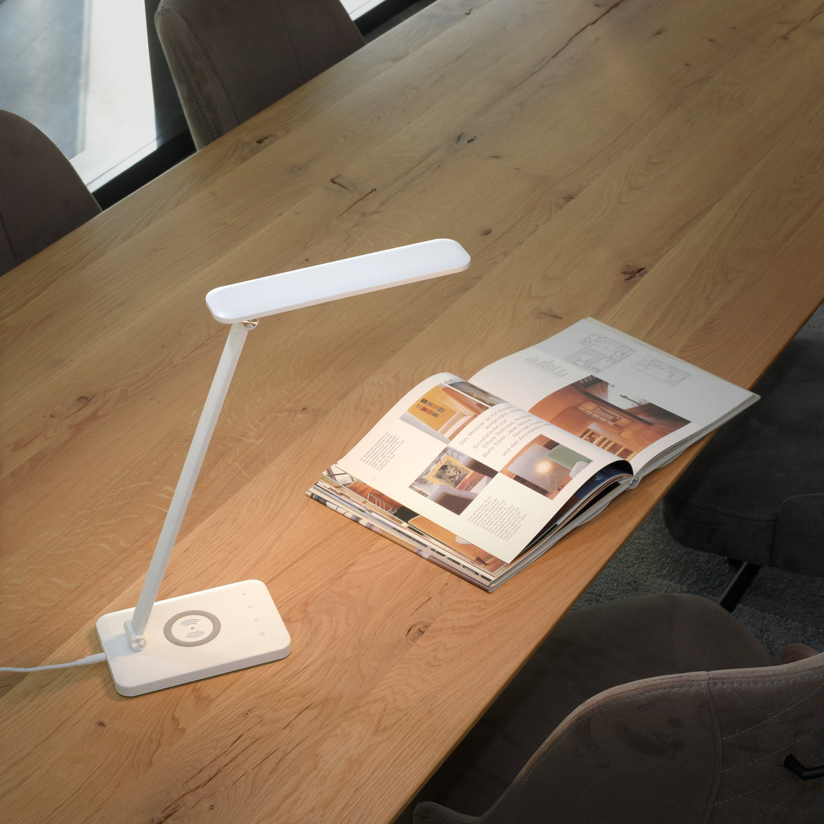 Mise en ambiance sur table en bois avec lampe allumée éclairant un magazine ouvert.
