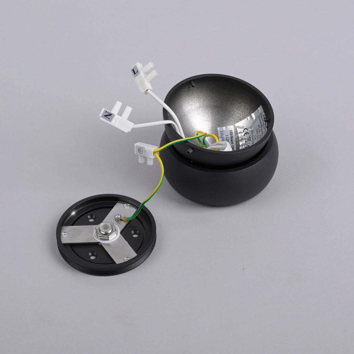 Pièces démontées du plafonnier noir, platine de fixation, module LED et fils électriques sur fond gris.