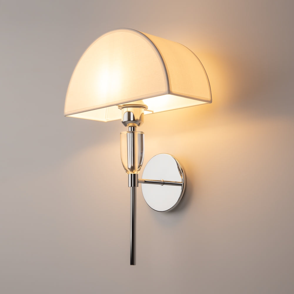 Vue de trois quarts de l'applique fixée au mur, halo lumineux doré projeté alentour.