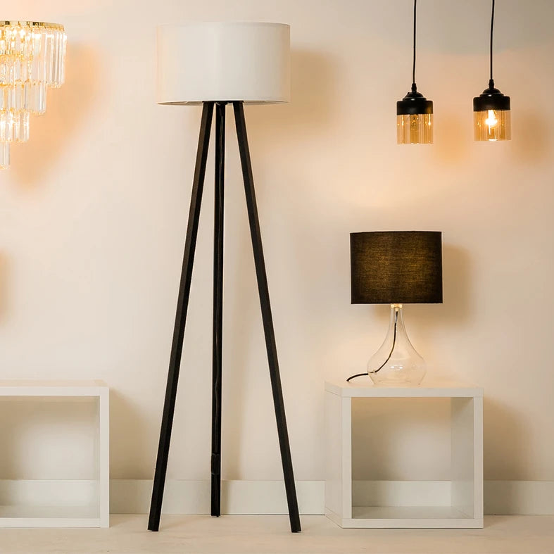 Lampadaire trépied noir dans un salon, entouré d'autres luminaires en ambiance