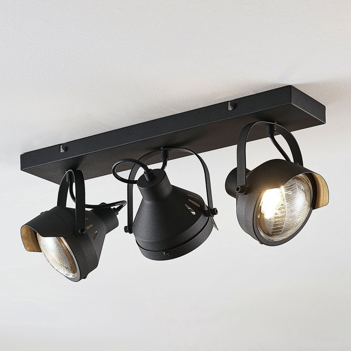 Trois spots noirs orientables fixés sous une base rectangulaire, vus de dessous.