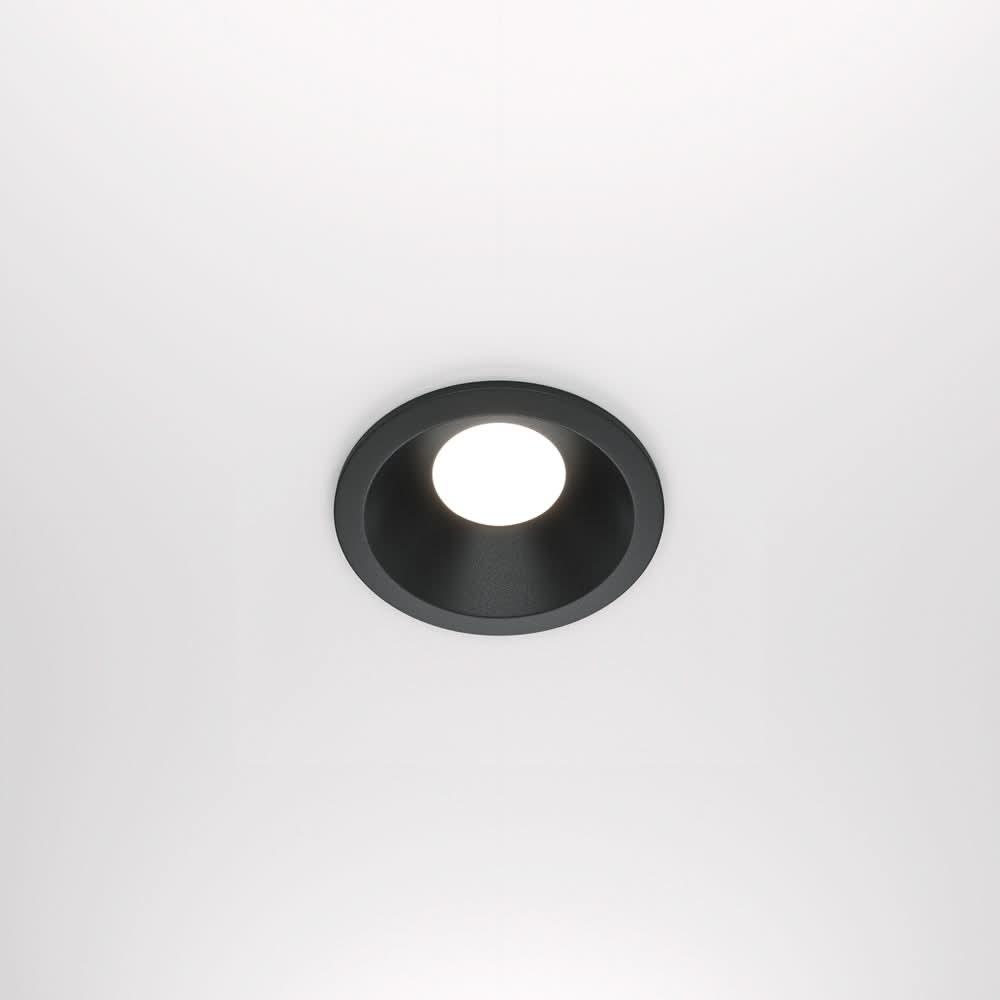 Vue de face d'un spot encastré rond noir allumé sur un plafond blanc