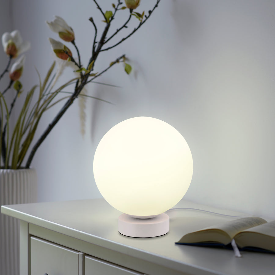 Lampe sphérique allumée posée sur une commode, près d'un livre ouvert et de branches fleuries.