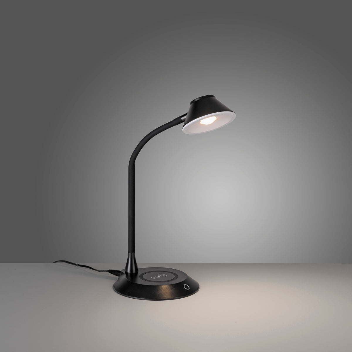 Lampe à poser noire éclairée sur fond gris, montrant sa lumière chaude