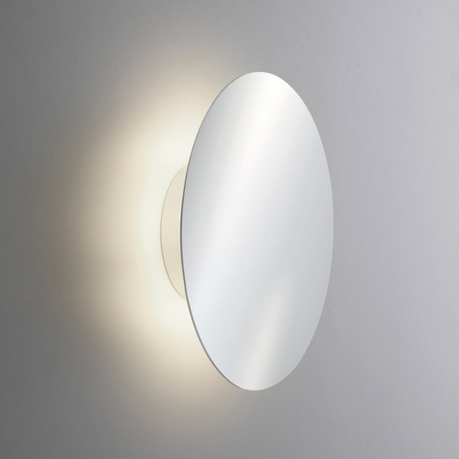Gros plan de l'applique ovale allumée projetant un halo lumineux sur le mur.