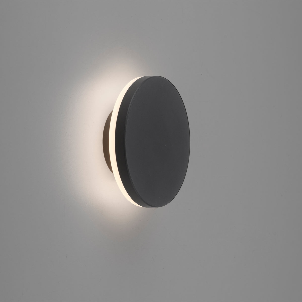 Applique ronde allumée sur mur gris, halo lumineux diffus autour du disque.