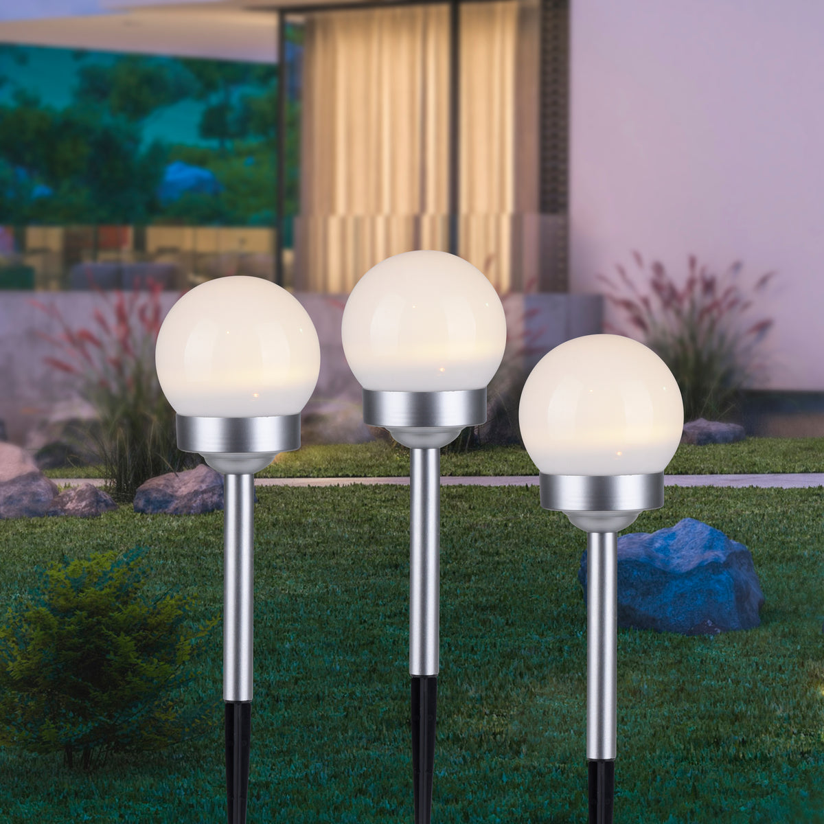 Mise en ambiance nocturne de trois piquets lumineux plantés dans une pelouse de jardin