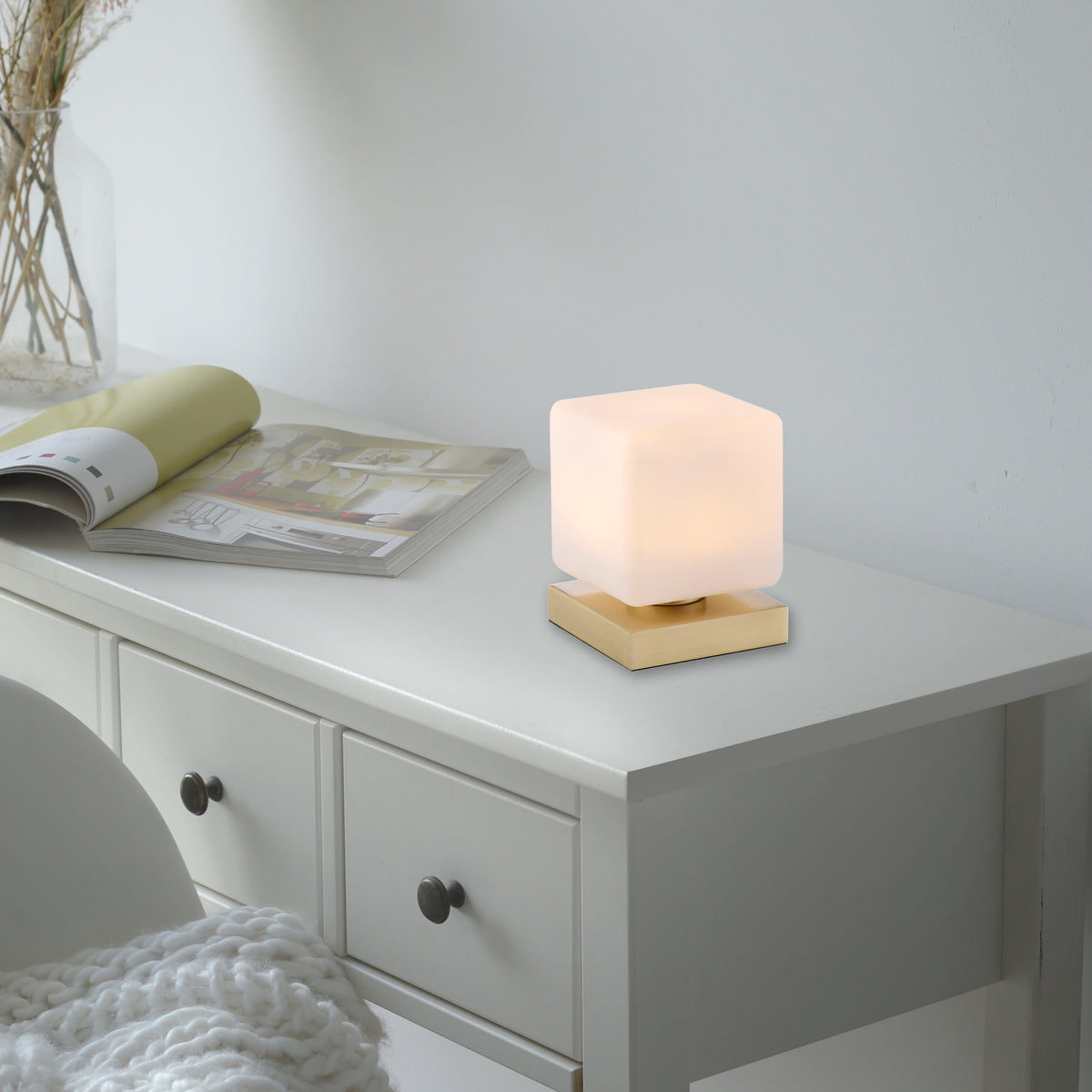 Mise en ambiance sur une commode blanche, lampe allumée près de magazines et d'un plaid.