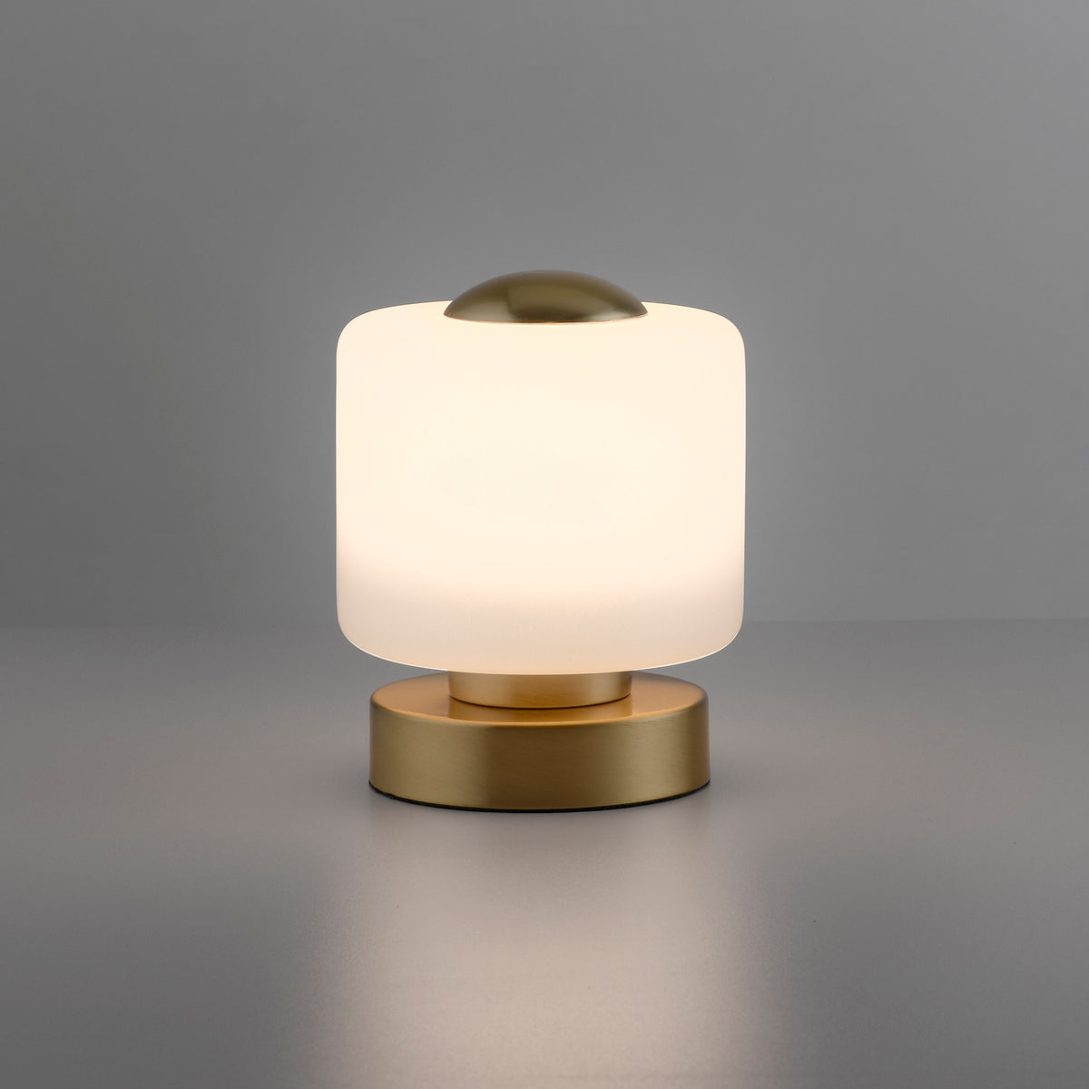 Lampe allumée sur fond gris, halo chaud à travers le verre opalin cylindrique.