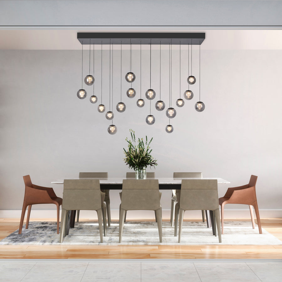 Suspension allumée au-dessus d'une table blanche avec chaises beiges et plante.