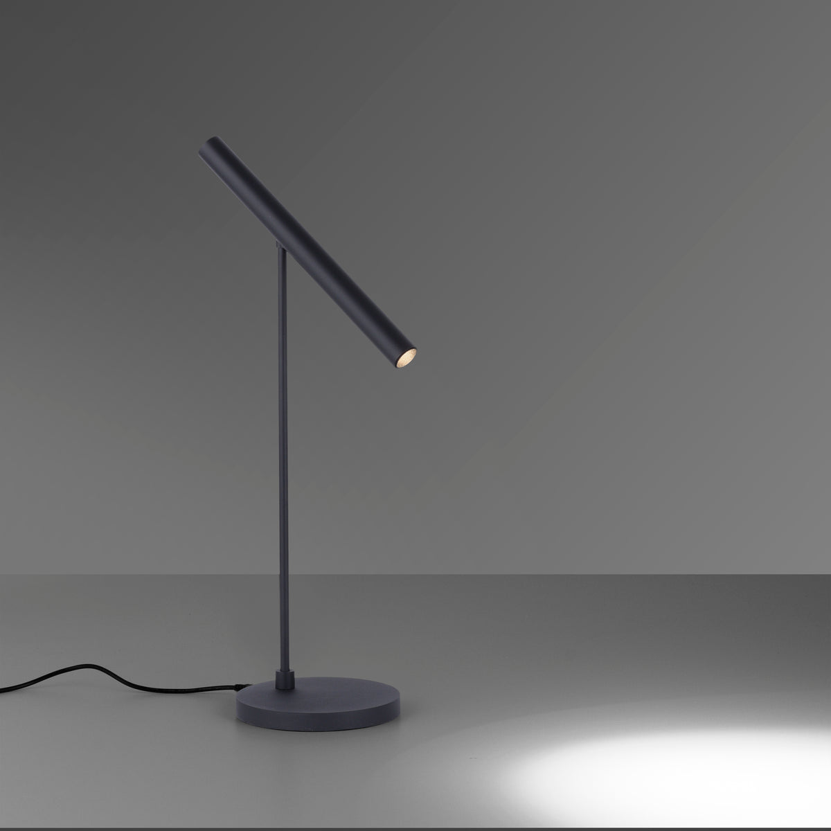 Lampe noire sur fond gris, câble visible et éclairage dirigé vers le bas.