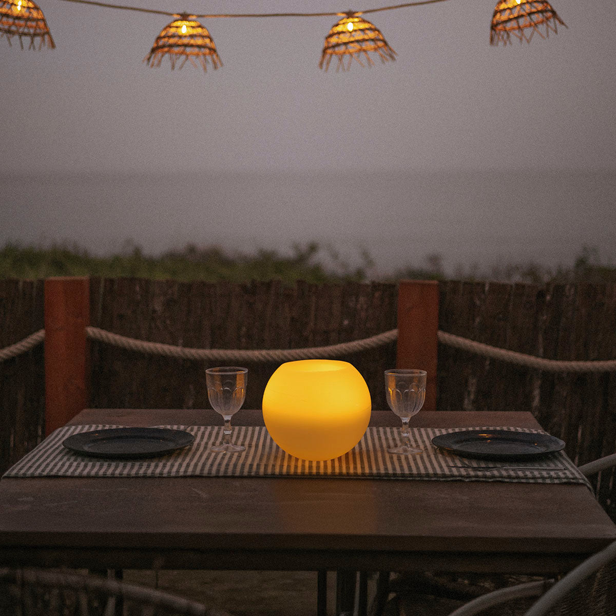 Lampe boule lumineuse posée sur table dressée, ambiance terrasse en soirée
