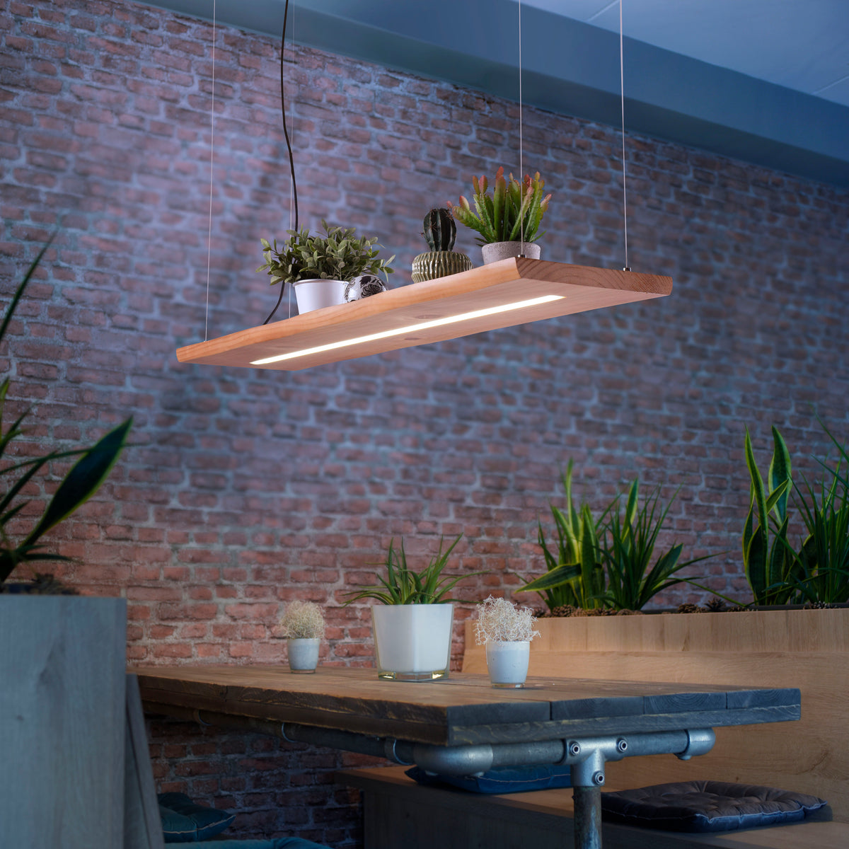 Mise en ambiance au-dessus d'une table en bois, briques rouges et plantes posées sur le luminaire