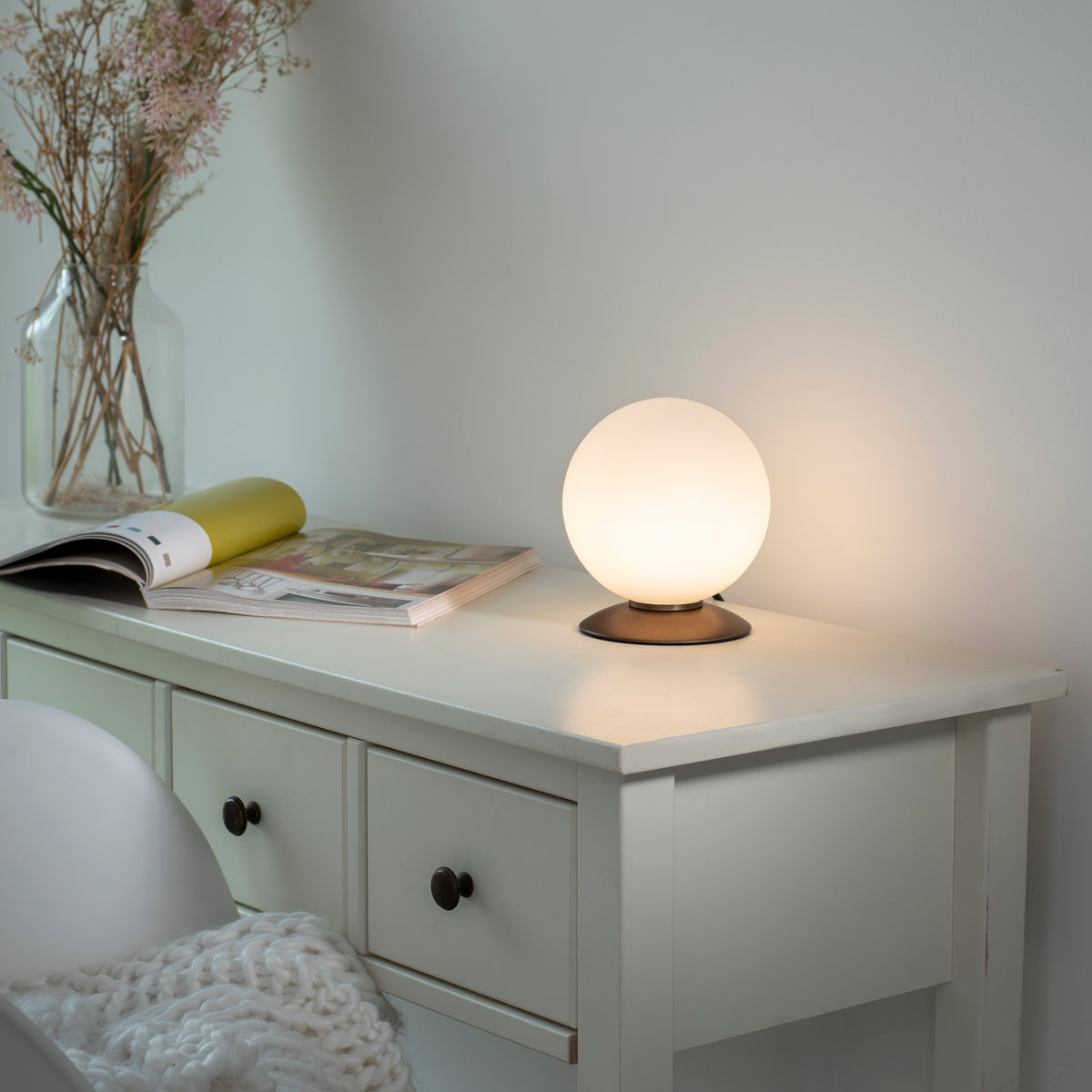 Mise en ambiance allumée sur une commode blanche, lumière chaude tamisée