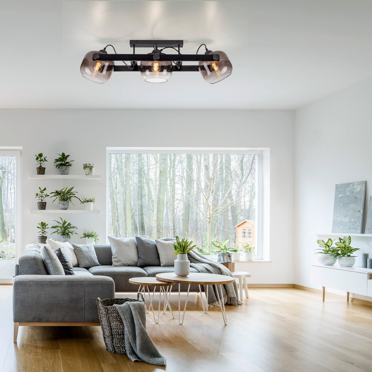 Mise en ambiance dans un salon lumineux, plafonnier allumé au-dessus d'un canapé gris.