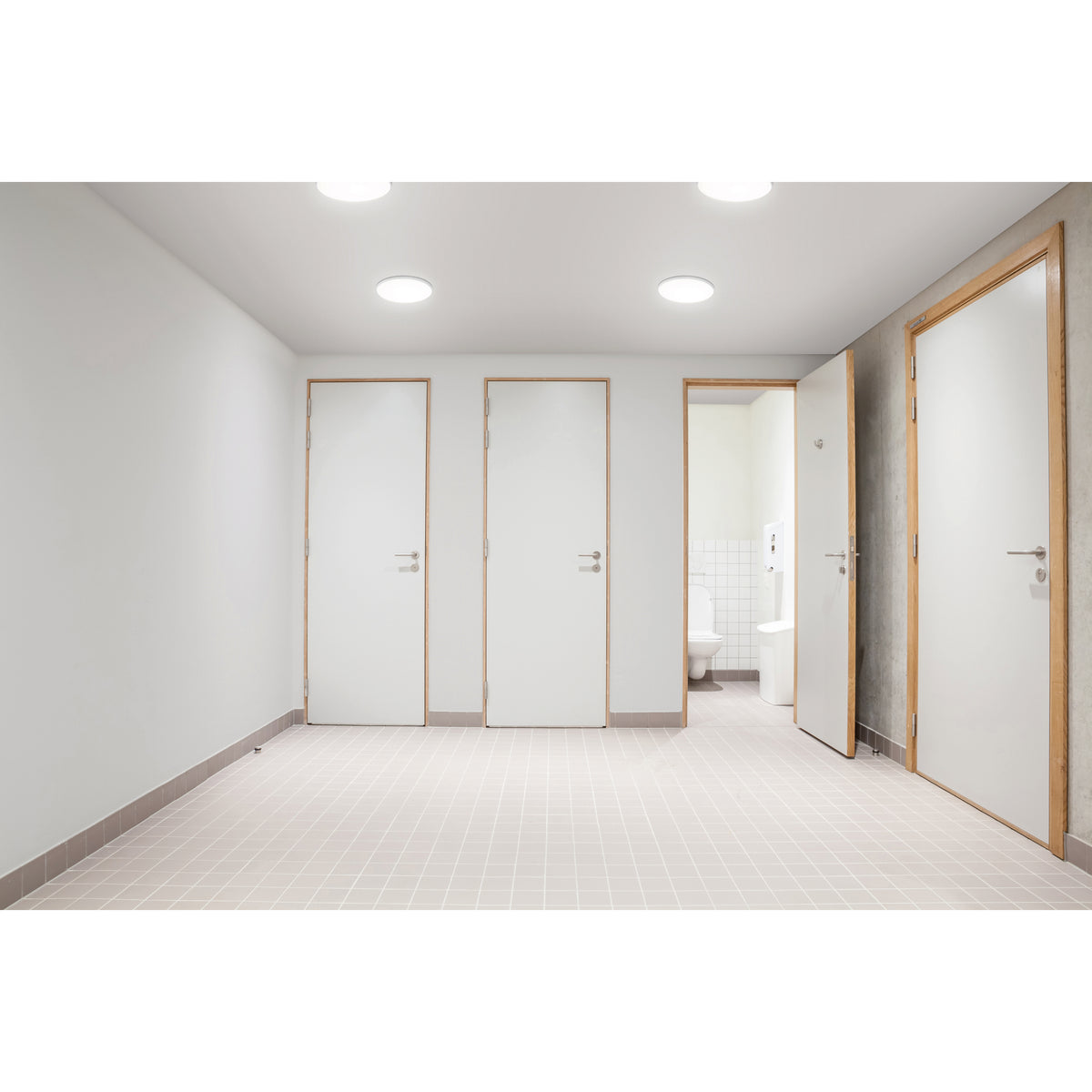 Couloir de sanitaires avec plusieurs plafonniers ronds allumés au plafond
