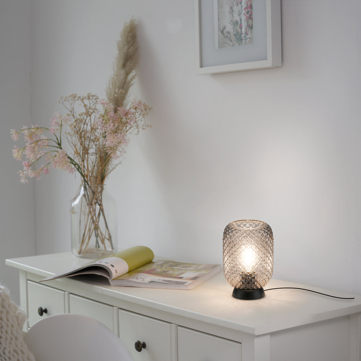 Mise en ambiance sur une commode blanche avec magazine et vase de fleurs séchées.