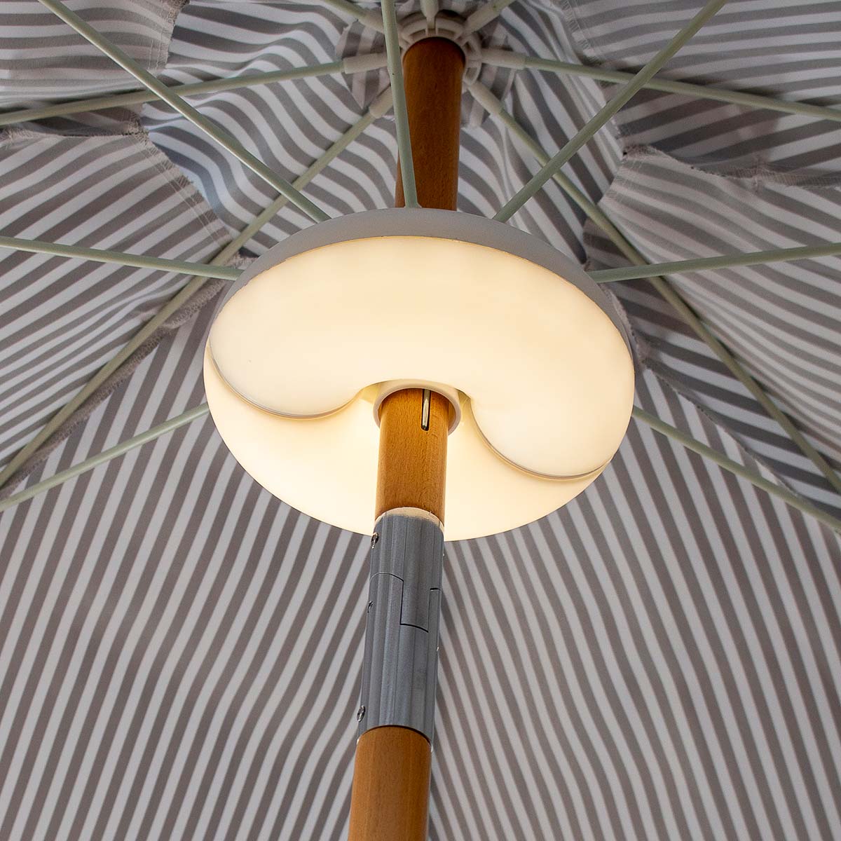 Vue en contre-plongée sous un parasol rayé, fente du luminaire autour du mât