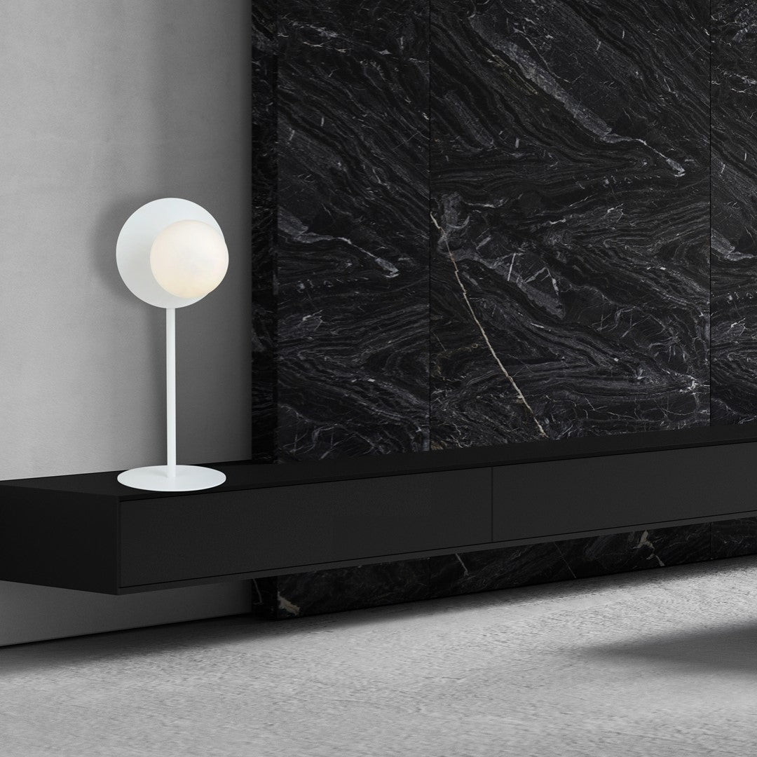 Mise en ambiance : lampe blanche posée sur un meuble noir devant un mur de marbre.