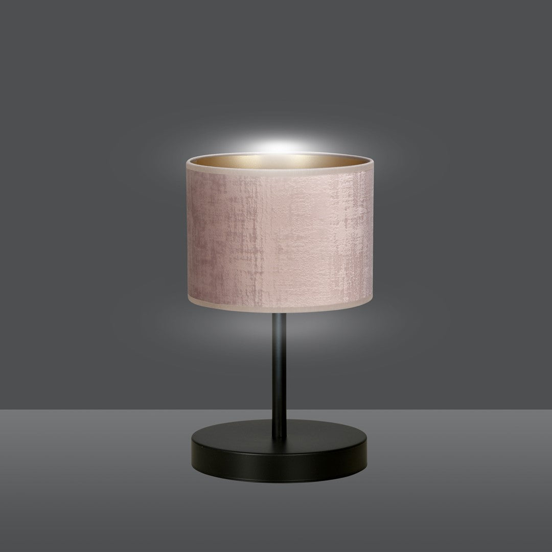Lampe allumée diffusant une lumière chaude, abat-jour rose et base noire sur fond gris foncé.