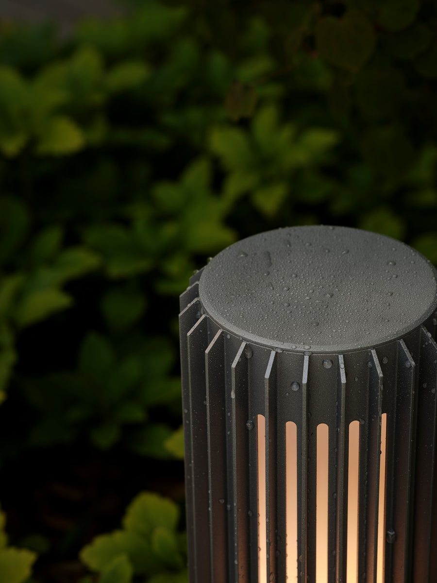Détail du sommet de la borne avec gouttes d'eau, finition noire et fentes lumineuses.