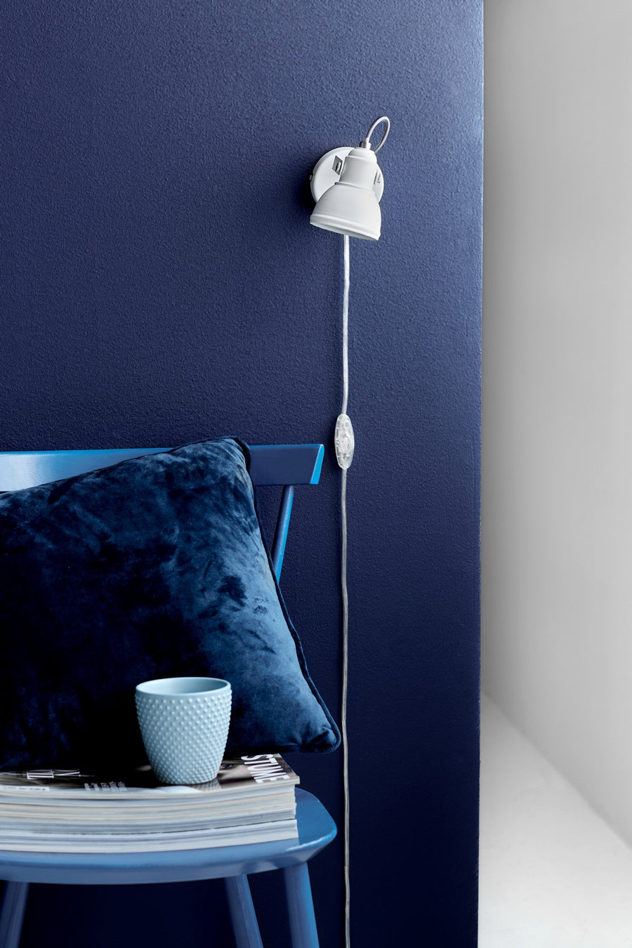 Applique blanche fixée sur mur bleu, cordon avec interrupteur pendant le long du mur.